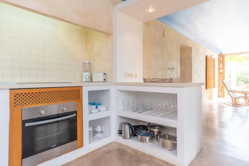 A kitchen counter with an oven, open shelves, and a bright dining area beyond.