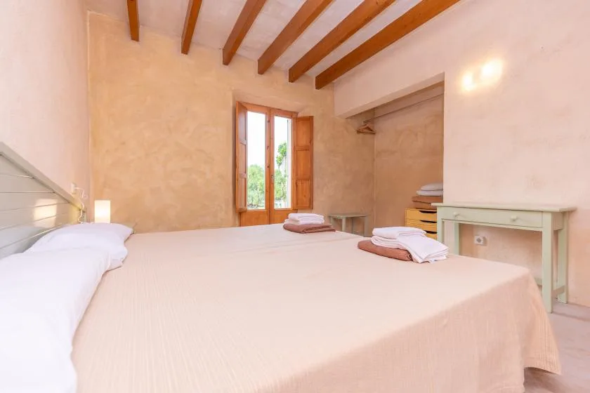 A bedroom with a large bed, wooden ceiling beams, and a window.