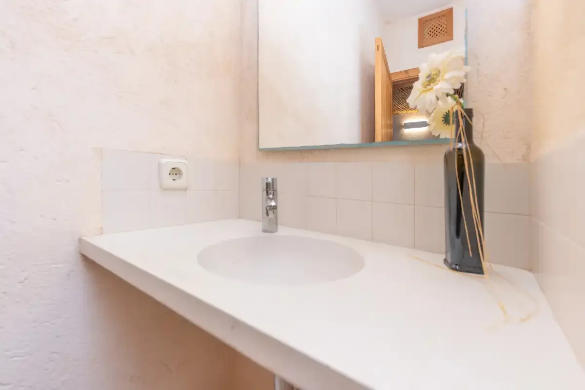 A bathroom vanity with a basin, wall mirror, and vase of flowers.