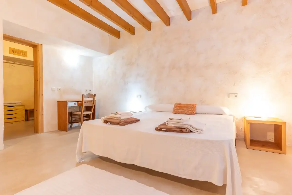 A bright bedroom with a large bed and exposed wooden ceiling beams.