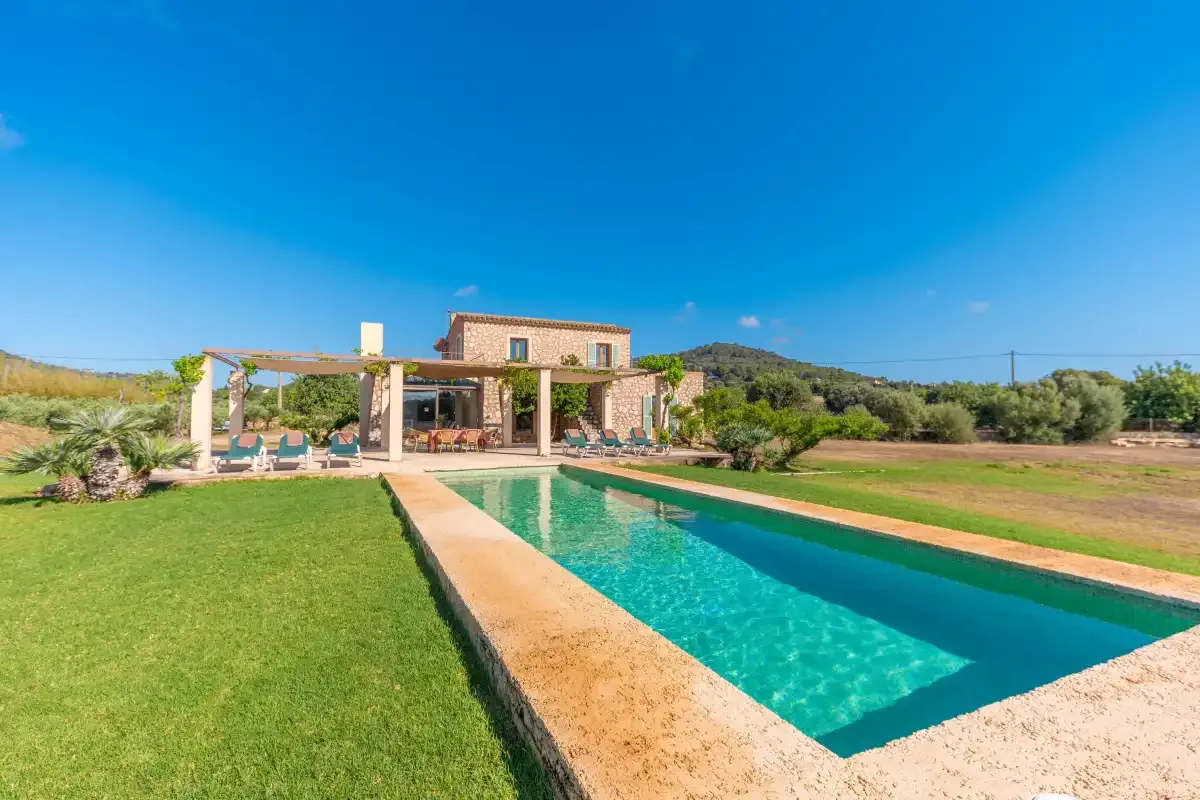 A swimming pool beside a lawn, with a low stone building in the background.