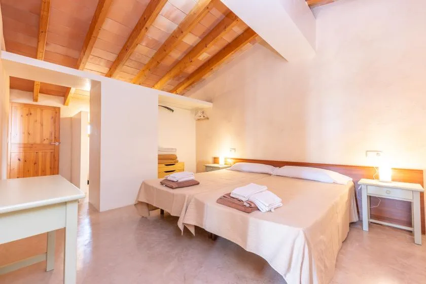 A bedroom with two beds, bedside tables, and exposed wooden ceiling beams.