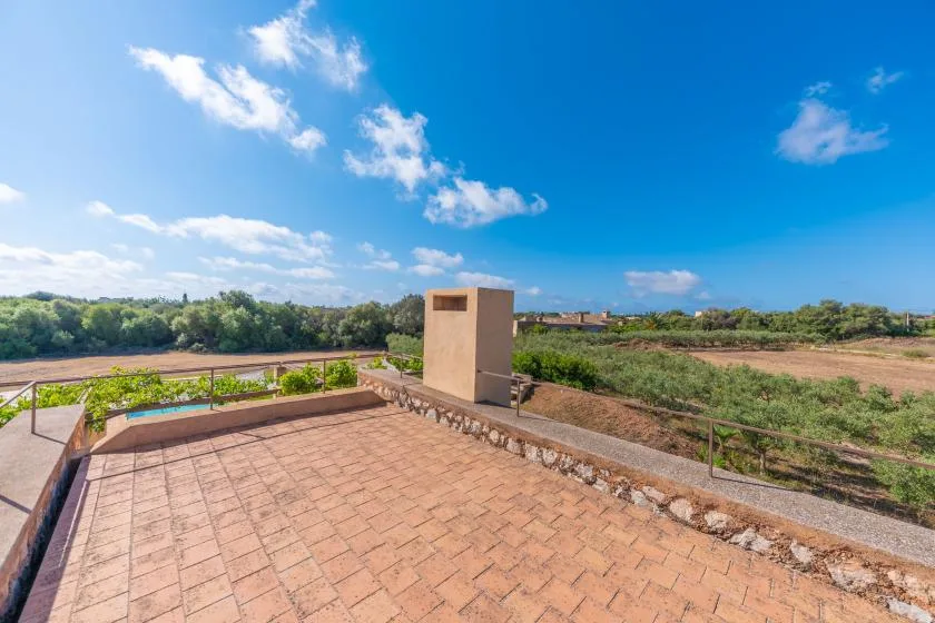 A tiled rooftop terrace overlooks green fields beneath a bright blue sky.