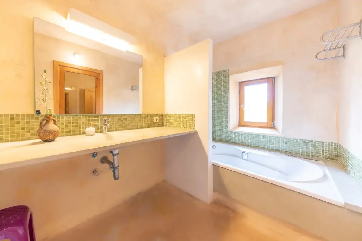A bathroom with a long sink counter and a bathtub beneath a window.