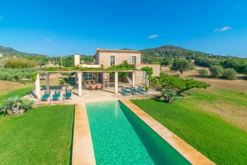 An outdoor swimming pool and lawn sit in front of a shaded patio.