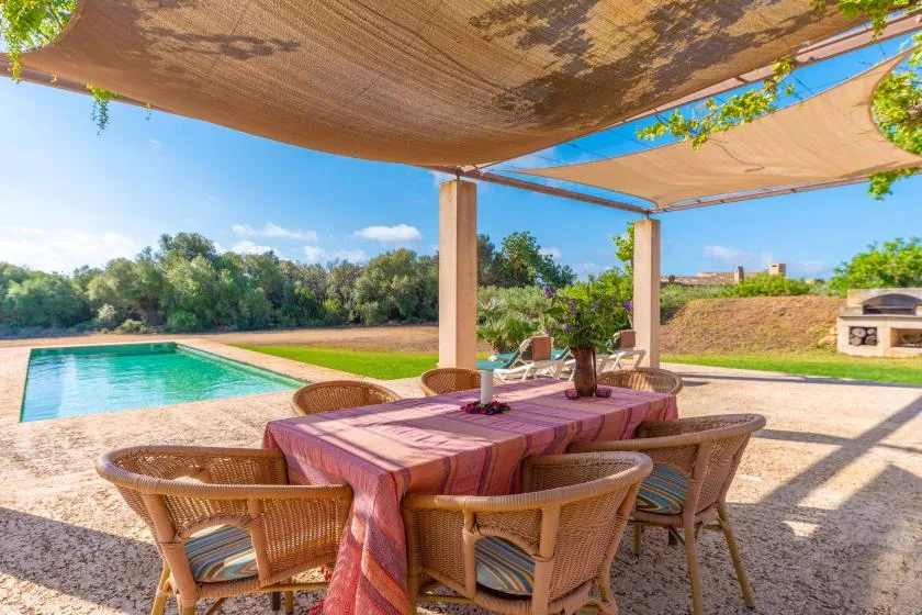 An outdoor dining area sits beneath a shaded pergola beside a swimming pool.