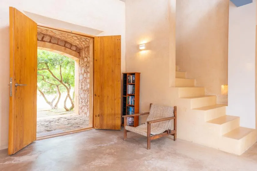 A bright interior entryway opens to a garden beside a staircase and wooden chair.