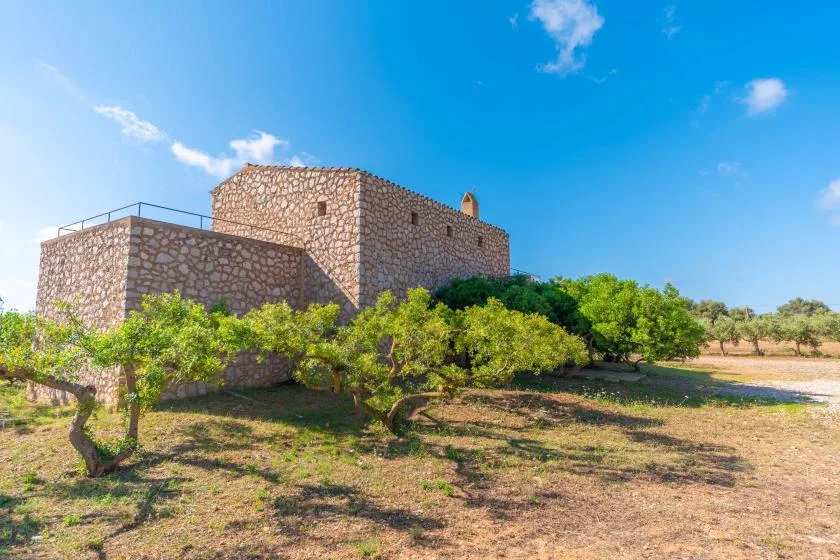 A stone building stands among trees beneath a clear blue sky.