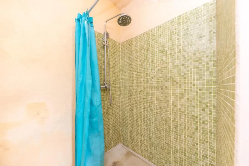 A tiled shower area with a turquoise curtain and round overhead showerhead.