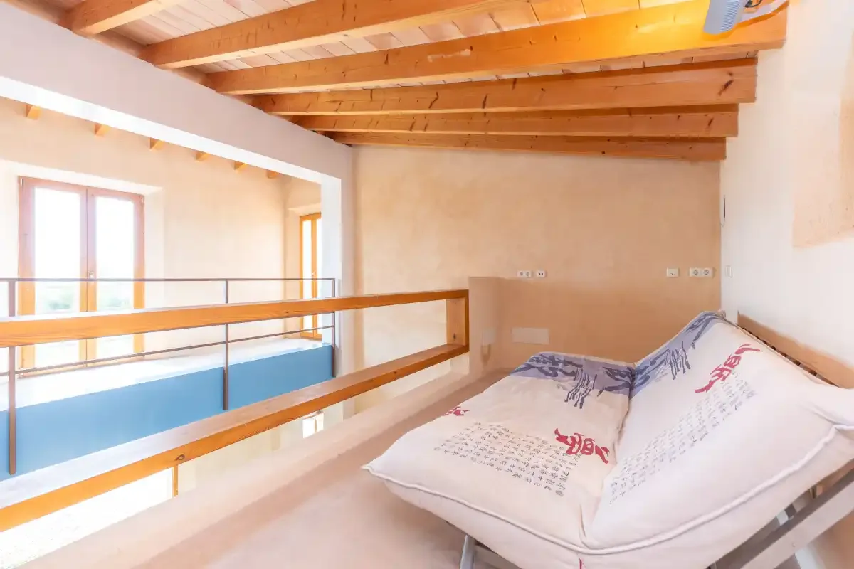 A loft bedroom with a bed beside a wooden railing overlooking the lower floor.