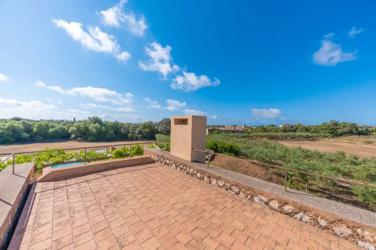 A tiled outdoor terrace overlooks green fields beneath a bright blue sky.