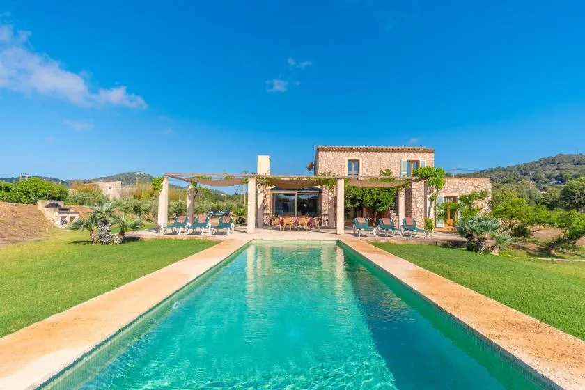 A long outdoor swimming pool leads toward a stone house and landscaped grounds.