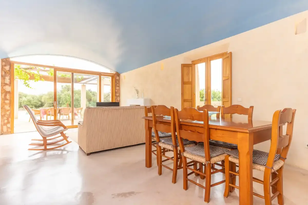 A bright living and dining area has a wooden table beside large windows.