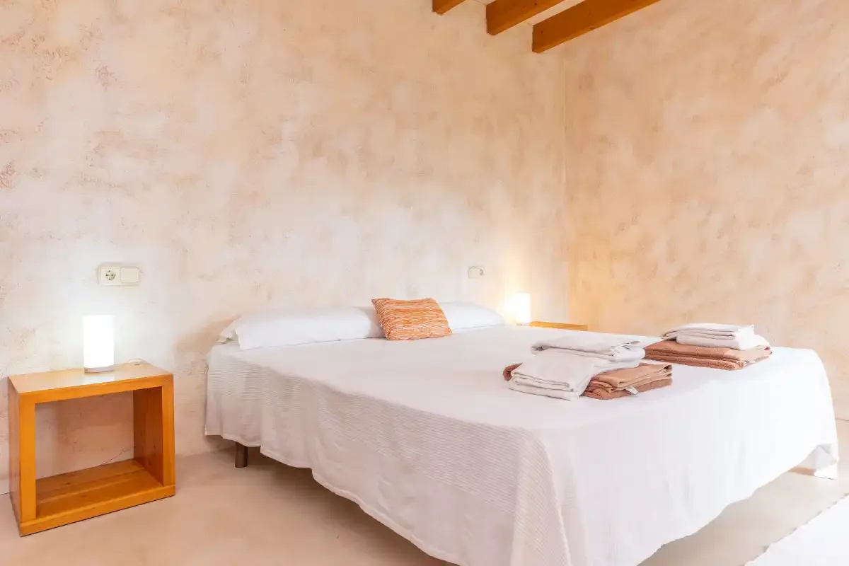 A bedroom with a neatly made bed and wooden ceiling beams.