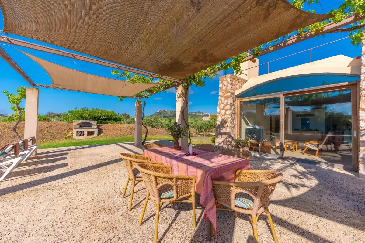 A shaded outdoor dining area with a table and seating beside a glass-fronted room.