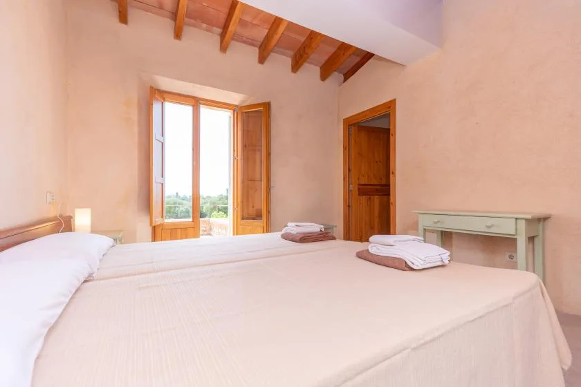 A bedroom with a large bed, exposed ceiling beams, and open balcony doors.