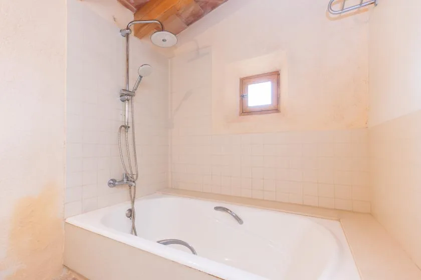 A bathroom with a bathtub, wall-mounted shower, and small window.