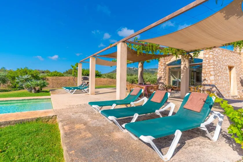 A sunny poolside patio has teal loungers beneath a shade canopy.