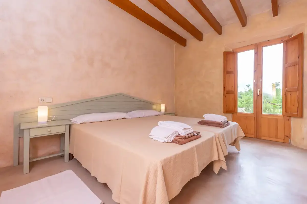 A bedroom with a double bed, folded towels, and an open window.