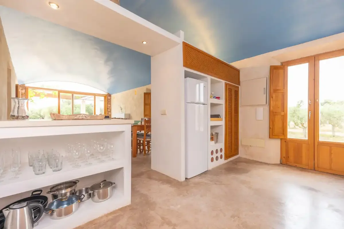 A bright kitchen with a counter, open shelving, and wooden doors.