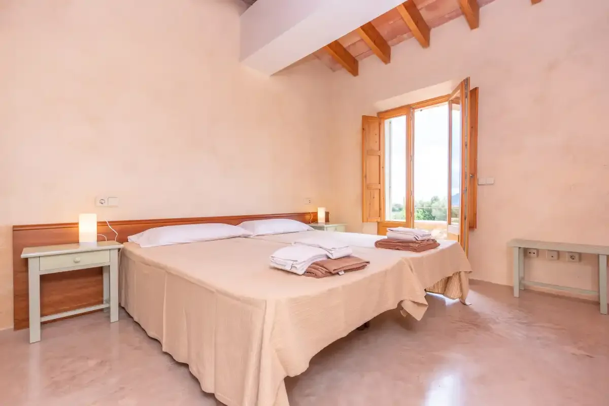 A bedroom with a large bed, bedside tables, and an open wooden window.