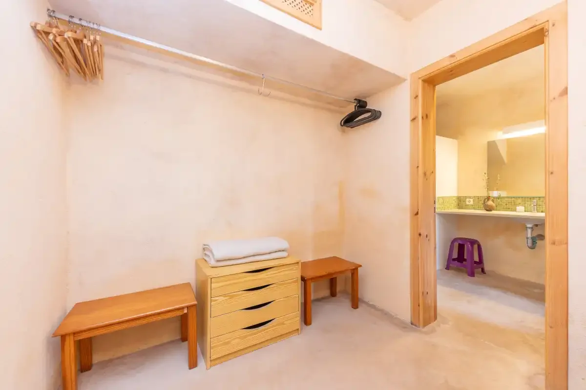 A simple dressing area with a clothes rail, wooden drawers, and a bathroom doorway.