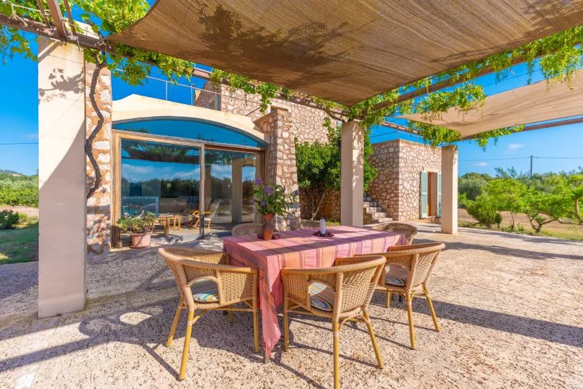 Outdoor dining area beneath a shade canopy, beside a stone-faced building.