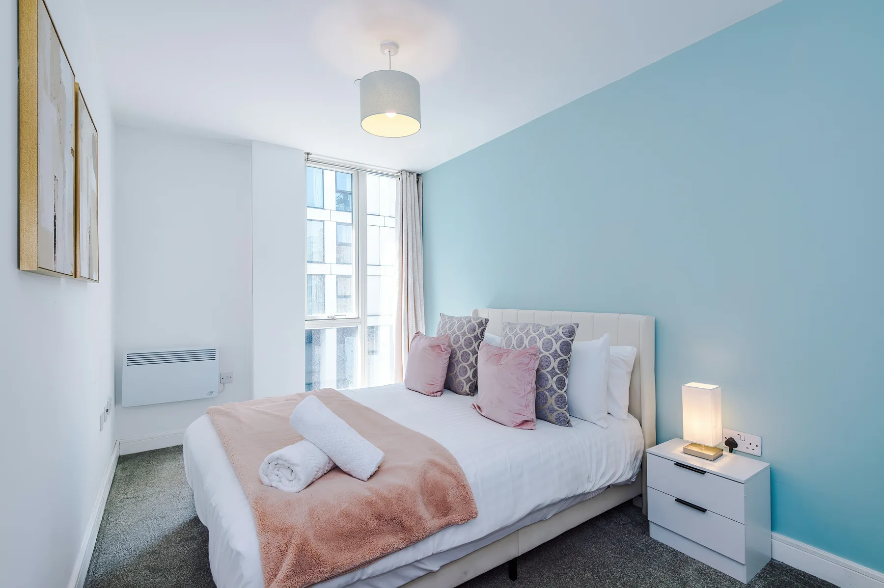 A bright bedroom with a neatly made bed beside a large window.