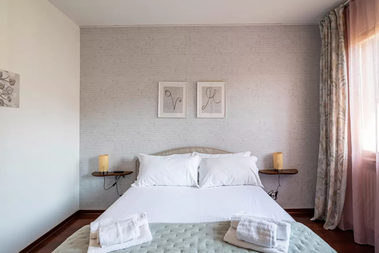 Un dormitorio con una cama bien tendida y cuadros enmarcados sobre ella.