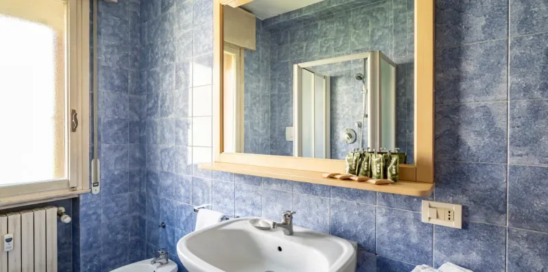 Un baño con azulejos, un lavabo y un espejo grande.