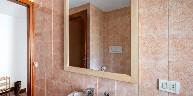 Pared de baño alicatada con un espejo grande y un lavabo.