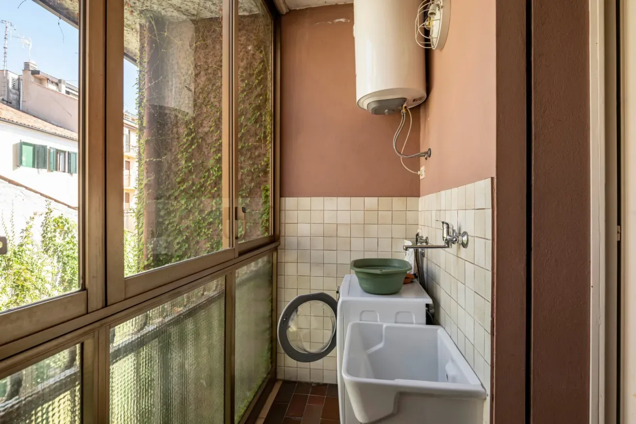 Una zona de lavandería estrecha tiene una lavadora, un fregadero de servicio y un calentador de agua.
