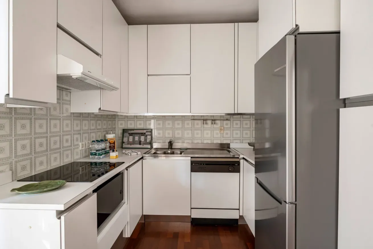Una cocina compacta con gabinetes blancos, azulejos estampados y electrodomésticos de acero inoxidable.