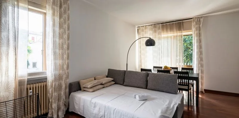 Un dormitorio con una cama, cojines grises y una mesa junto a la ventana.