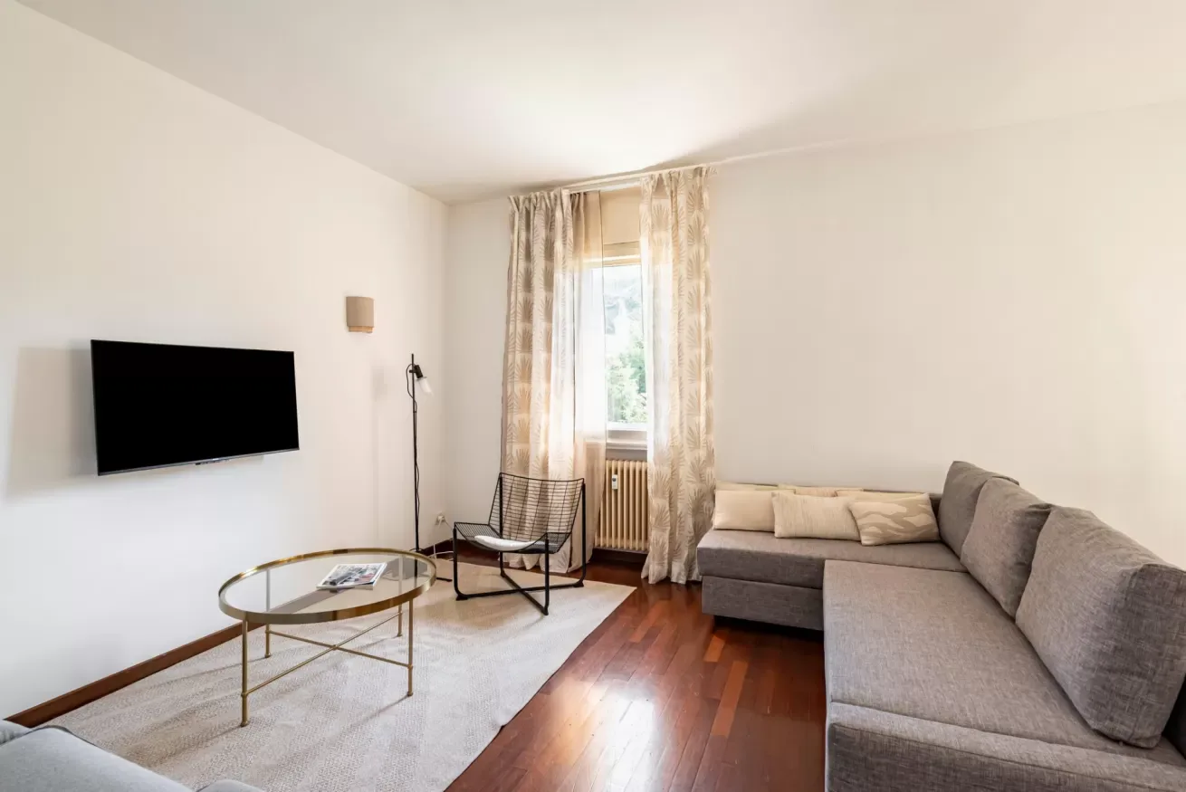 Una sala de estar con un sofá seccional gris, un televisor y una ventana con cortinas.