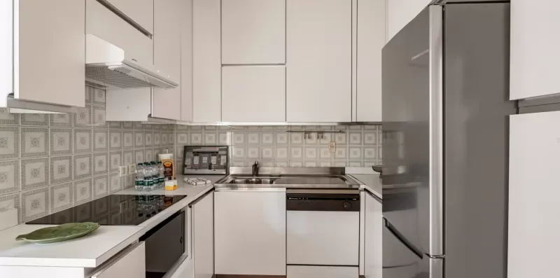 Una cocina moderna con gabinetes blancos, una placa de cocina y un refrigerador de acero inoxidable.