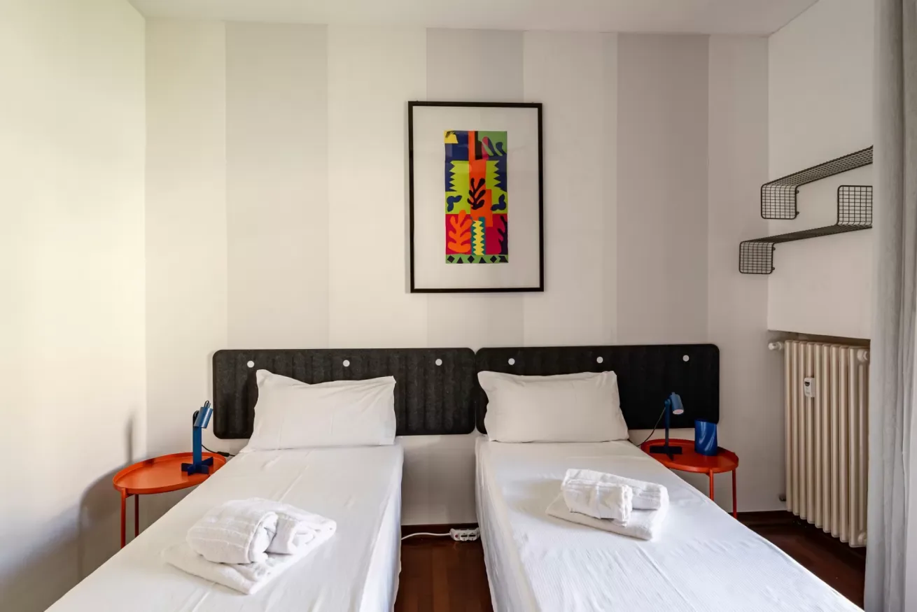 Un dormitorio con dos camas individuales y una obra de arte colorida sobre el cabecero.