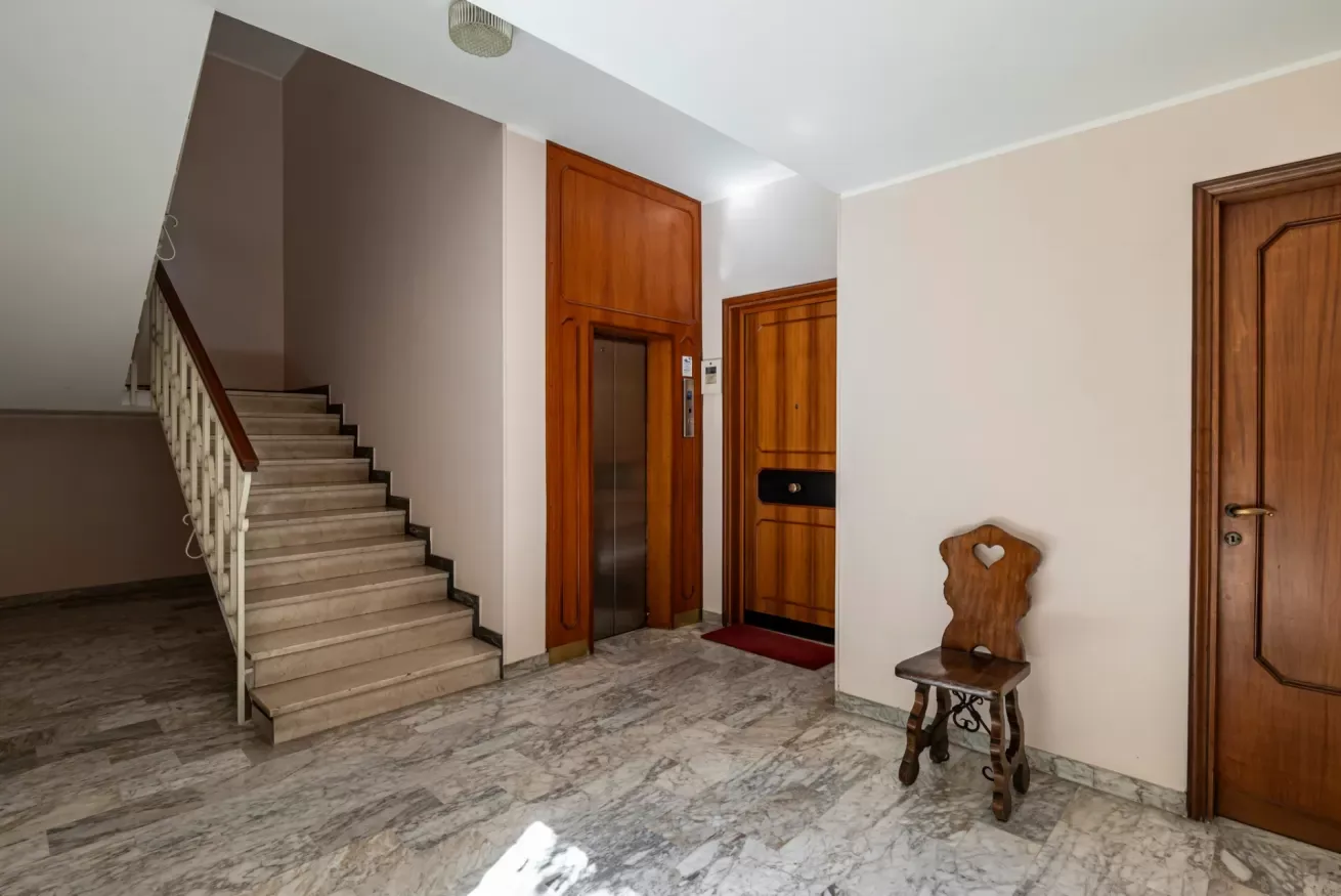 Un recibidor de apartamento con una escalera, puertas de madera y una silla pequeña.