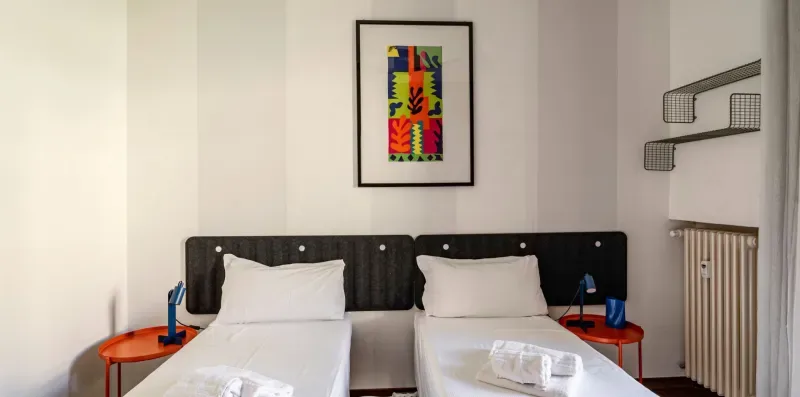 Un dormitorio con dos camas, ropa de cama blanca y una lámina enmarcada colorida.