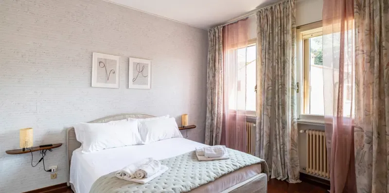 Un dormitorio con una cama bien hecha y ventanas altas con cortinas.