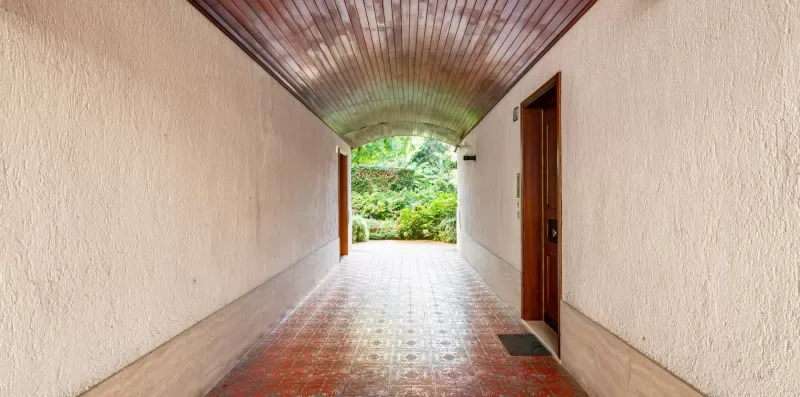 Un pasillo cubierto se abre hacia un jardín verde.