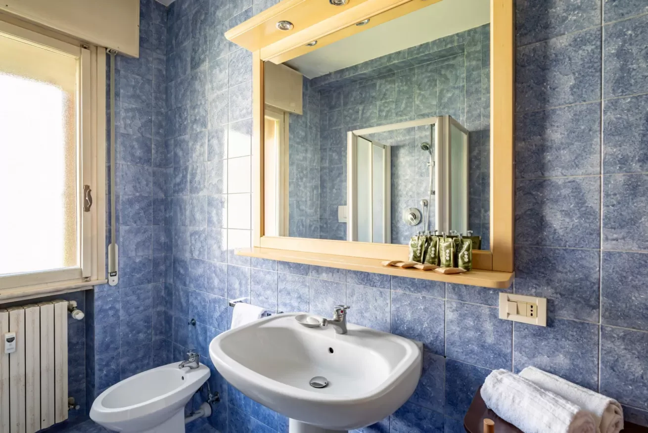 Un baño con azulejos azules, lavabo, espejo y ventana.