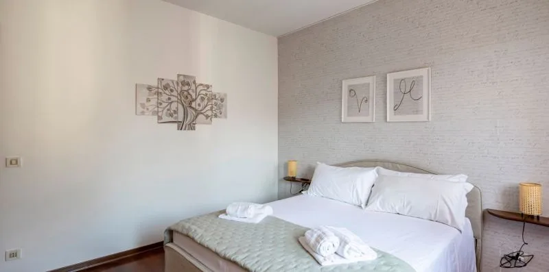 Un dormitorio con una cama, ropa de cama blanca y cuadros en las paredes.