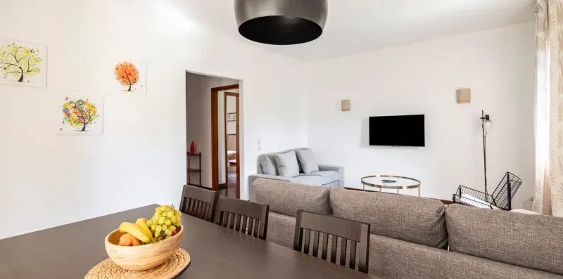 Una luminosa sala de estar y comedor con asientos, un televisor en la pared y una mesa de comedor.