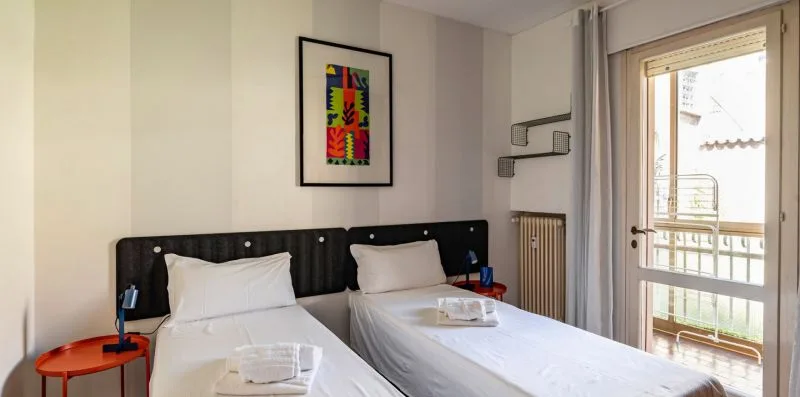 Un dormitorio con dos camas, una obra enmarcada y una puerta de vidrio que da a un balcón.
