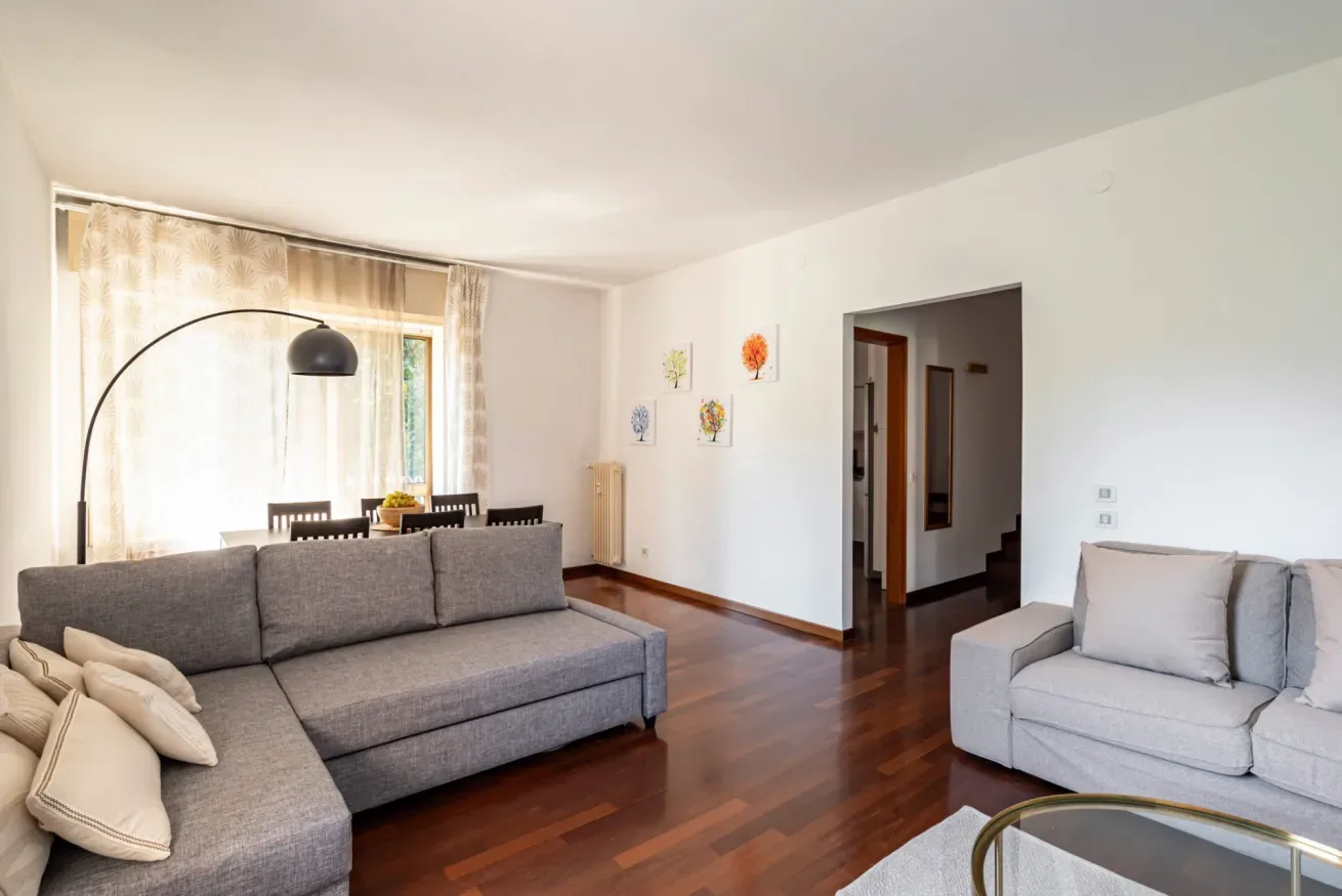 Una sala luminosa con asientos grises, una lámpara de pie curva y una ventana grande.