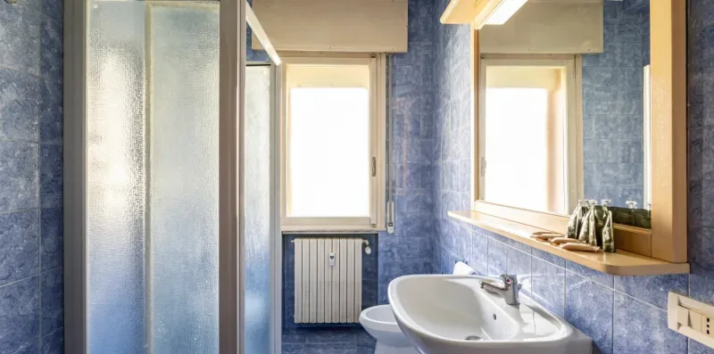 Un baño con azulejos azules, lavabo, espejo y ducha de vidrio esmerilado.