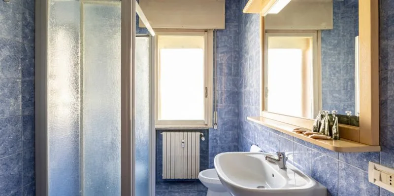 Un baño con azulejos azules, lavabo, espejo y ducha con vidrio esmerilado.