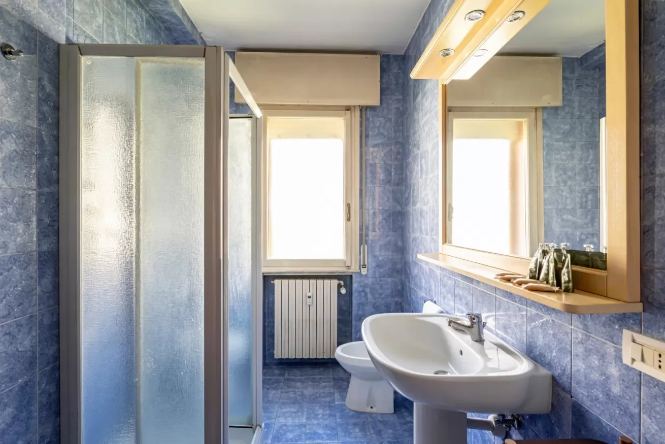 Un baño con azulejos, ducha, lavabo y ventanas luminosas.