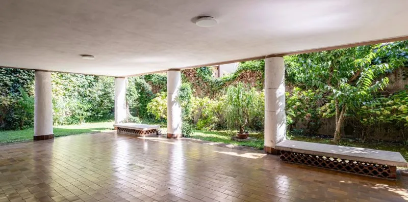 Un patio cubierto con suelo de baldosas se abre a un jardín frondoso.